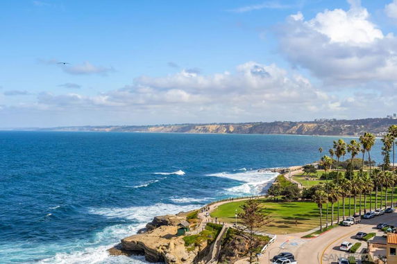 Panoramic view of a coastal landscape with cliffs, ocean, and palms.
