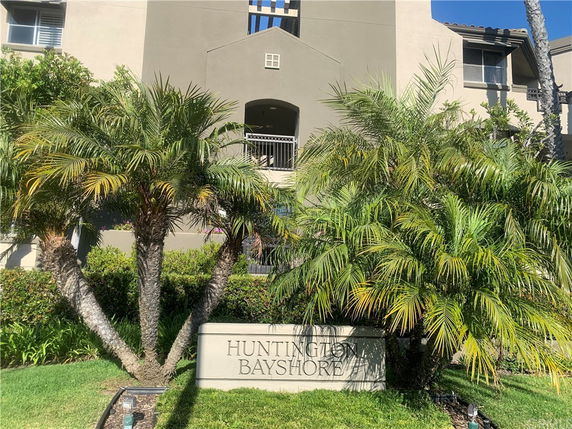 Front view of a multi-story building with a sign reading 'Huntington Bayshore' surrounded by palm trees.