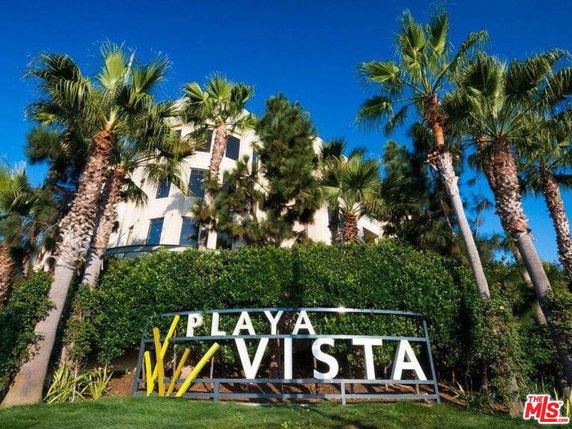 Front view of a building partially obscured by palm trees and greenery with a sign reading 'Playa Vista'.