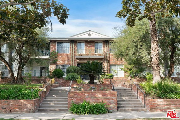 Front view of a two-story brick building with a central entrance and surrounding greenery.