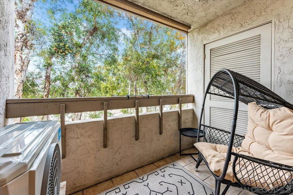 View from a small balcony with outdoor chair and trees visible beyond the railing.
