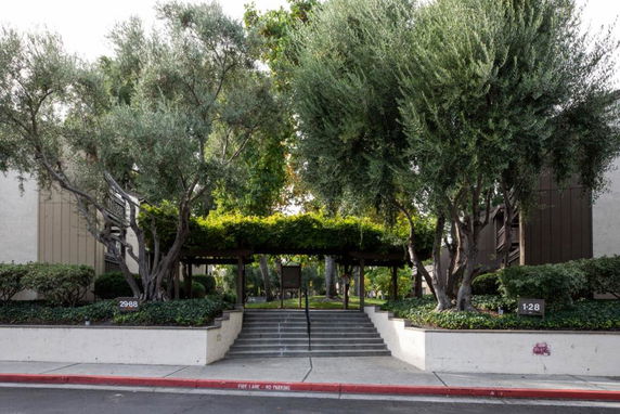 Front view of a building with stairs leading up, surrounded by trees and greenery.