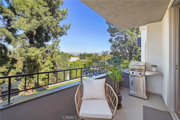 Balcony view with outdoor seating and grill, overlooking trees and neighborhood.