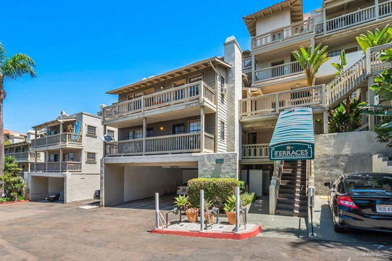 Front view of a multi-story residential building with balconies and stairway entrance.