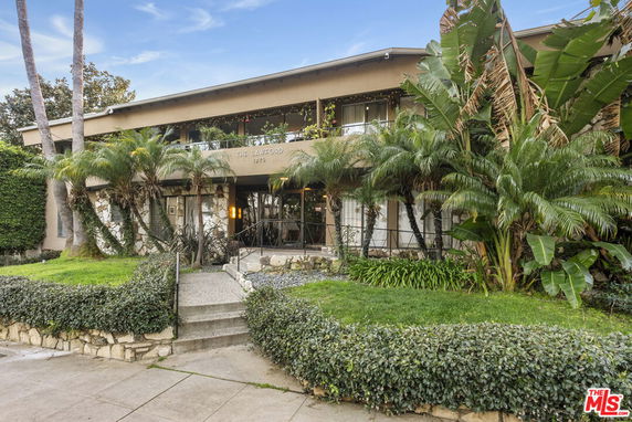 Front view of a two-story building with a flat roof and tropical landscaping.