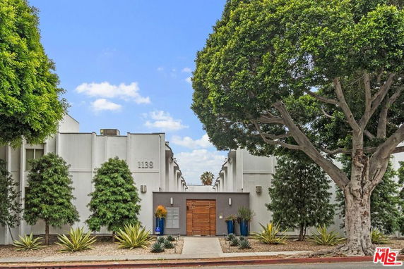 Front view of a modern building with a gated entrance and tall trees.
