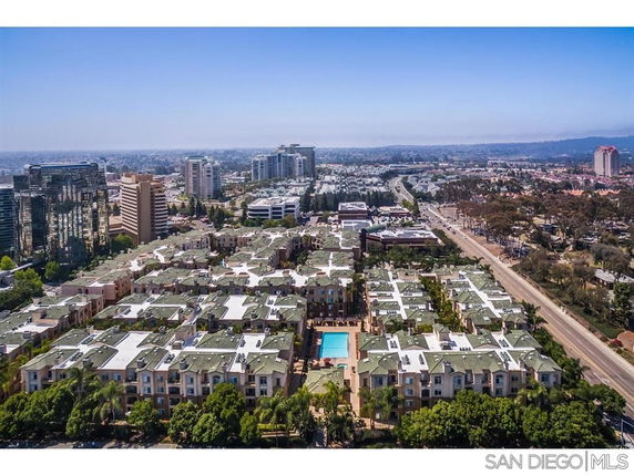 Wide aerial view of an urban residential area with multiple buildings and a swimming pool in the center.