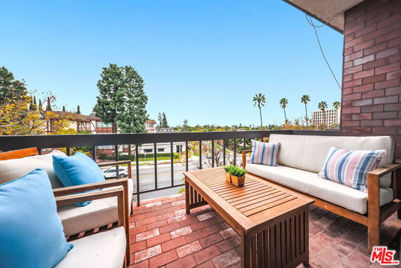 Balcony with seating area overlooking trees and distant buildings.