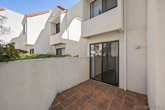 Front view of a multi-story house with sliding glass doors and tiled patio area.