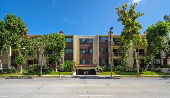 Front view of a multi-story apartment building with balconies and surrounding trees.