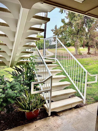 Outdoor staircase with white railings leading to the upper area, surrounded by greenery.