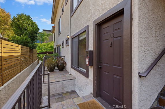 Side view of a multi-story building entrance with a tiled pathway and brown door.