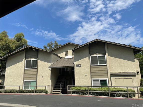 Front view of a two-story residential building with tan stucco exterior and brown roof.
