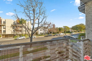 View from a balcony overlooking a street with parked cars and buildings.