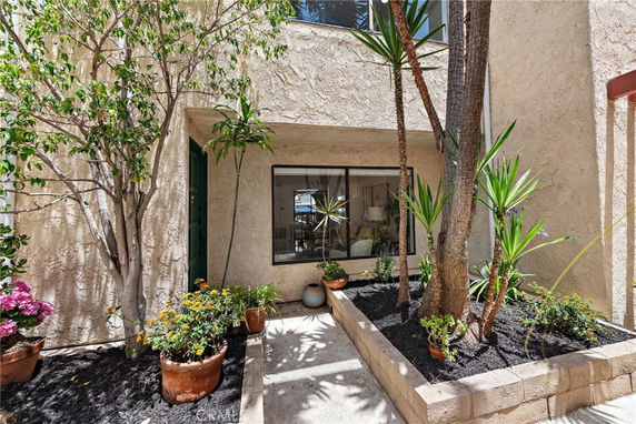 Front view of a house with a stucco exterior and a small garden area with potted plants.