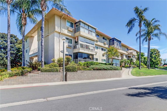 Front view of a multi-story apartment building with balconies and a landscaped front area.