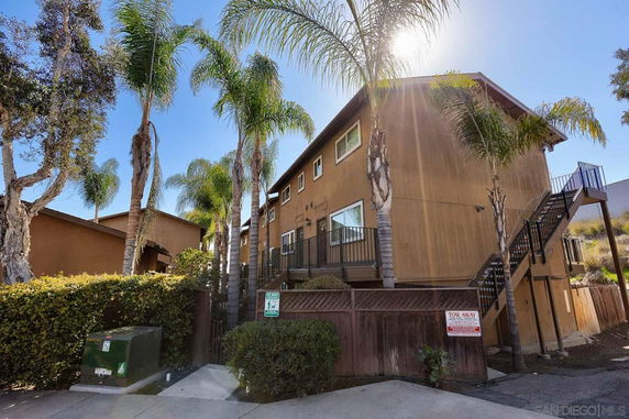 Front view of a two-story beige building with external staircases and palm trees.