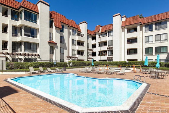 Outdoor swimming pool in front of a multi-story residential building with red tiled roofs.