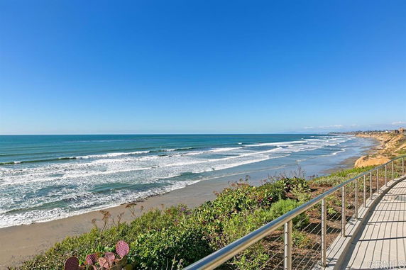 Panoramic view of a beach with waves and a walkway along the coastline.