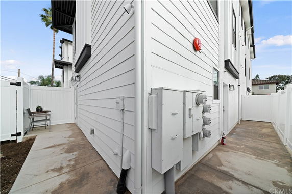 Side view of a white multi-story building with electrical meters and a small outdoor seating area.