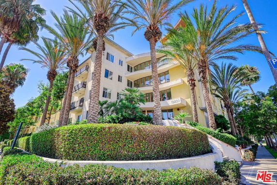 Front view of a multi-story apartment building with balconies and surrounded by palm trees.