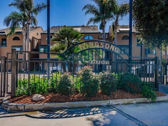 Front view of a residential complex with palm trees and gated entrance.
