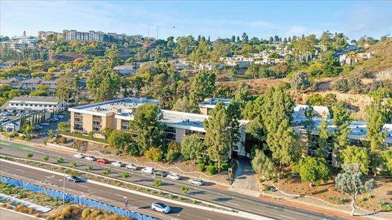 Aerial view of a mid-sized commercial building surrounded by trees, with roads and cars in the foreground.