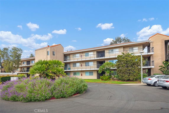 Front view of a three-story residential building with balconies and a landscaped area.