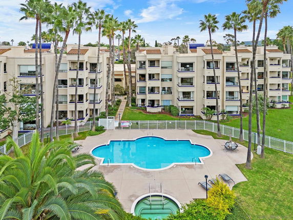 View of an apartment complex with a central swimming pool and surrounding palm trees.