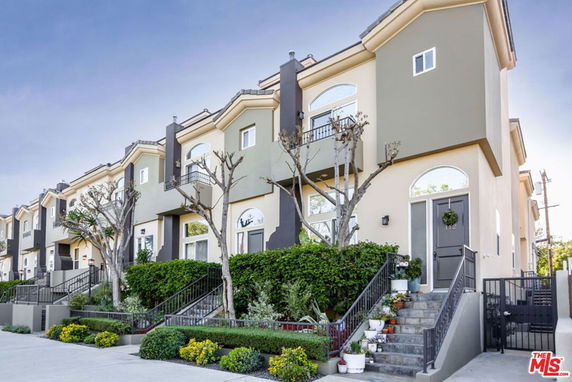Front view of a row of multi-story townhouses with balconies and stairs leading to the entrances.