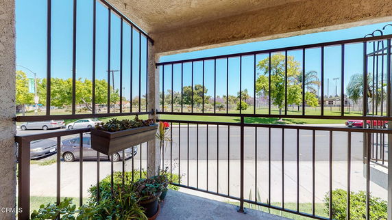 View from a balcony with metal railings overlooking a street and a park with trees.