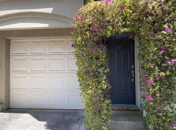 Front view of a house with a garage and a doorway arch covered with flowering vines.