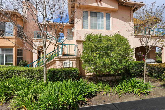 Front view of a two-story house with a staircase leading to the entrance, surrounded by greenery.