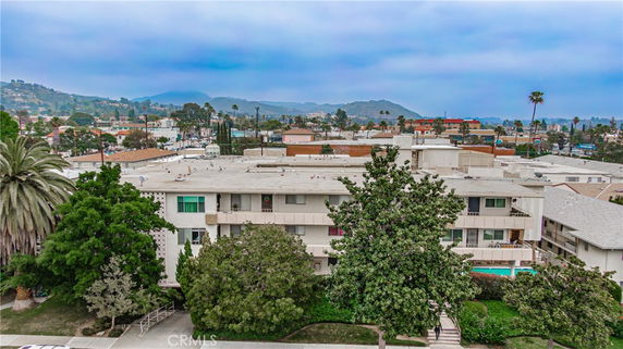 View of a multi-story residential building surrounded by trees with hills and urban landscape in the background.