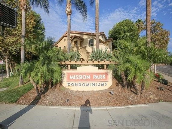Front view of a condominium building behind a landscaped area with palm trees and a sign reading 'Mission Park Condominiums.'