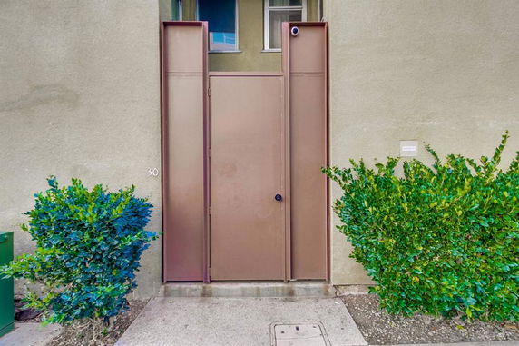 Front view of a building entrance with a metal door and surrounding plants.