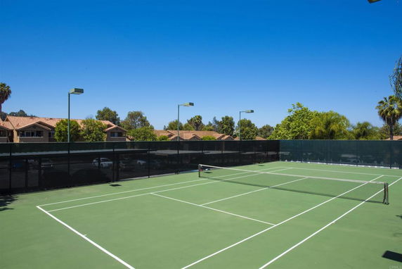 Tennis court with lighting surrounded by trees and houses.