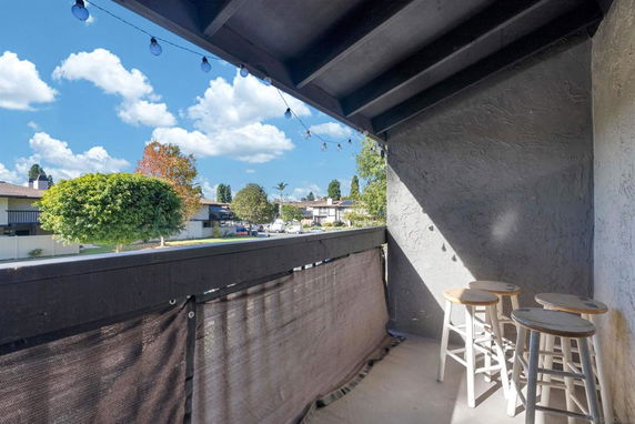 View from a covered balcony featuring outdoor stools and string lights, overlooking a residential neighborhood with trees and houses.
