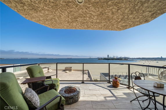 Panoramic view of a beach and ocean from a balcony with outdoor seating.