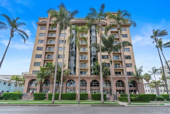 Front view of a multi-story residential building with balconies and palm trees.