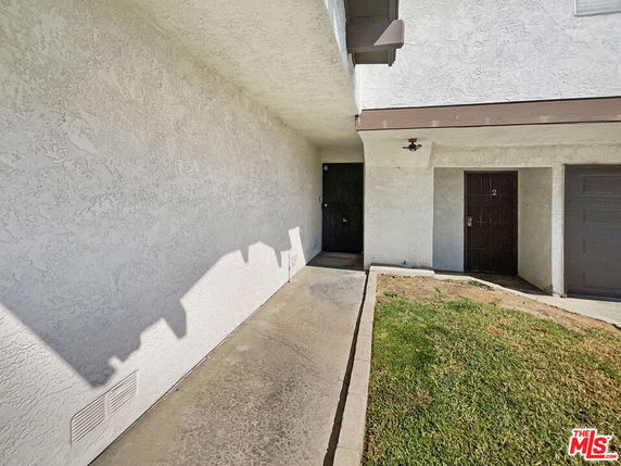 Front view of a building entrance with two doors and a small grassy area.