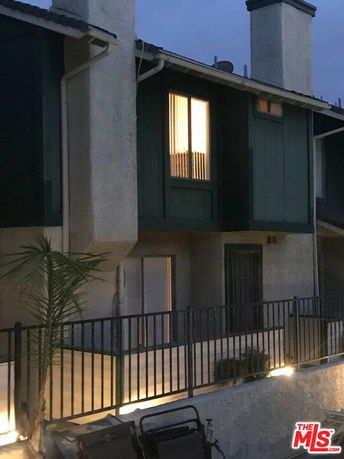 Front view of a multi-story house with illuminated windows and a fenced entrance.