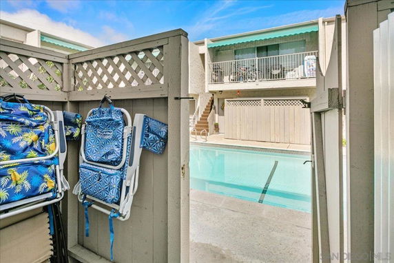 View of a residential swimming pool area with a fence and two-story building in the background.