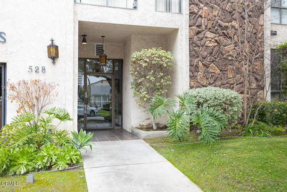 Front view of a building entrance with plants and address number 528.