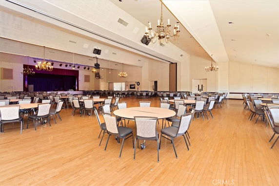 Large indoor banquet hall with round tables and chairs, chandeliers, and a stage.