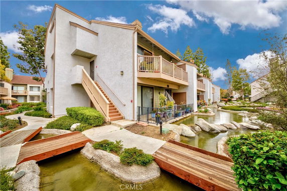 Front view of a multi-story building with balconies and a landscaped water feature.