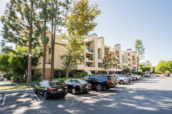 Front view of a multi-story apartment building with balconies and surrounding trees.