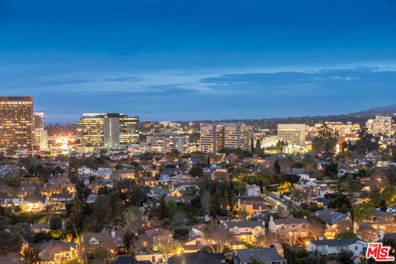 Panoramic view of a cityscape at dusk with illuminated buildings and houses.