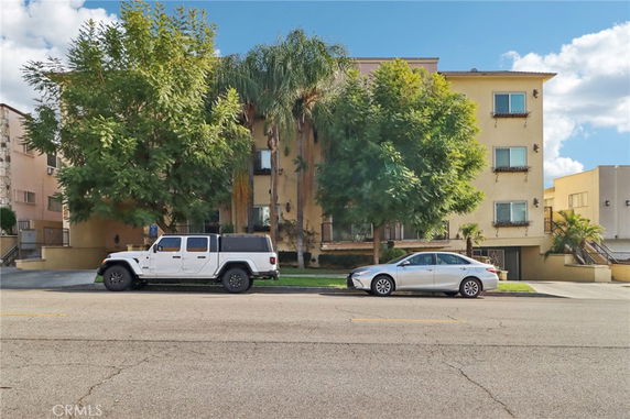 Front view of a multi-story residential building with trees and parked cars.