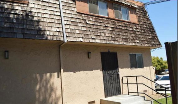 Front view of a two-story building with shingle roofing and metal railing steps.